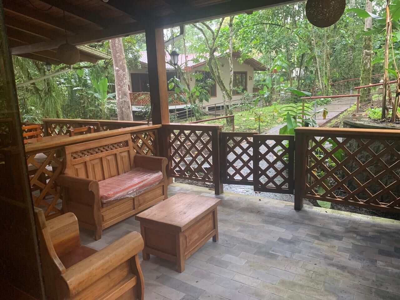 Una terraza de madera con un banco y una mesa, rodeada por un cerramiento de celosía, con vistas a un jardín exuberante.