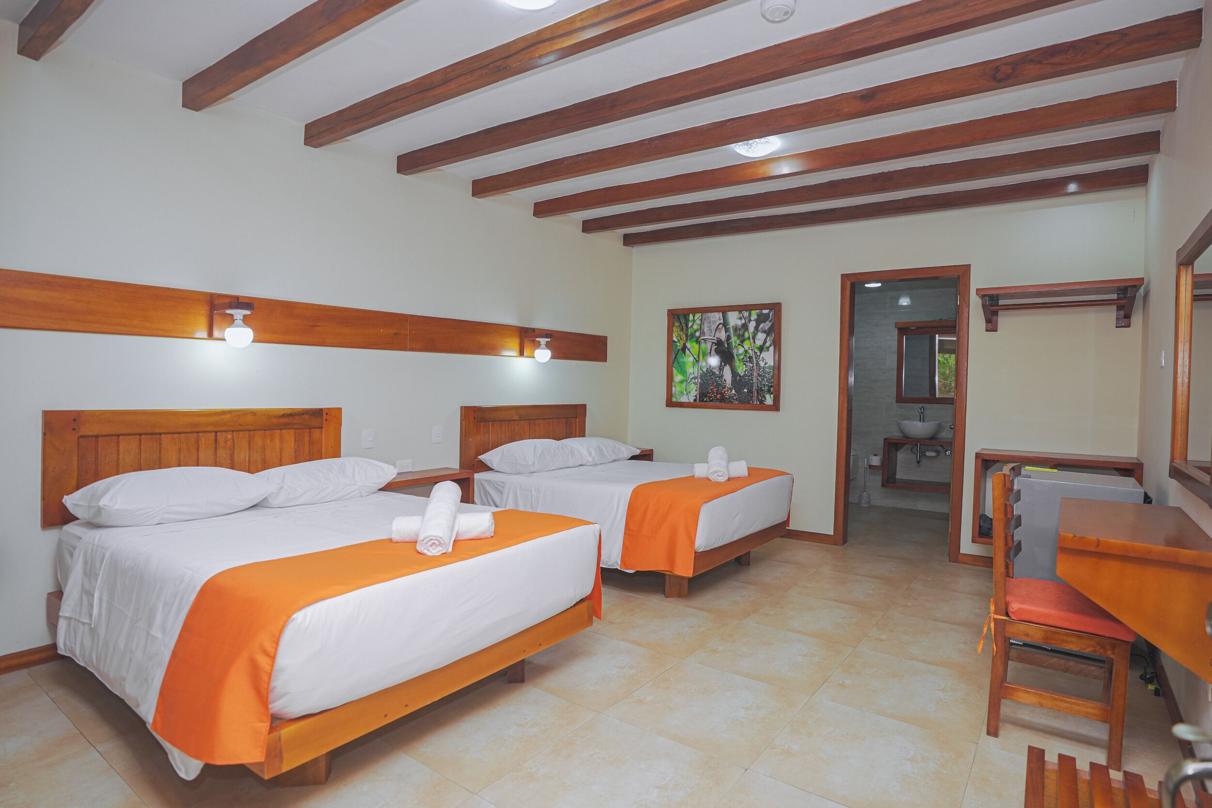 A hotel room with two beds, wooden beams on the ceiling, a desk, and a chair.