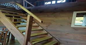 A wooden staircase leading to a loft area with a window overlooking greenery.