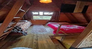A wooden interior with a loft bed, a window, and a wooden floor.