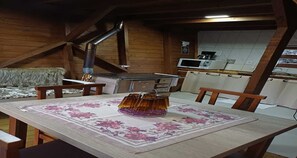 A wooden interior with a dining table, chairs, a fireplace, a kitchen area, and a sofa.