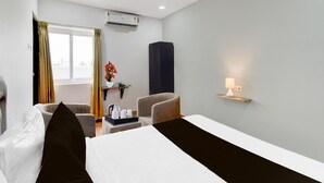 Een hotelkamer met een bed, twee stoelen, een klein tafeltje met een dienblad, een wandlamp en een airconditioning.