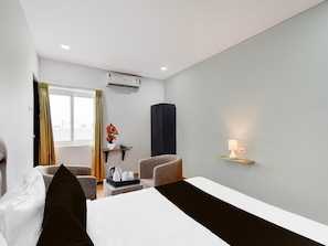 Ein Hotelzimmer mit einem Bett, zwei Stühlen, einem kleinen Tisch mit Tablett, einer Wandlampe und einer Klimaanlage.