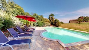 Une piscine avec des chaises longues et un parasol rouge.