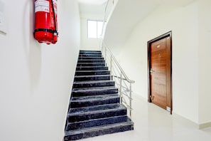 Una escala amb un extintor fixat a la paret, una porta de fusta i una finestra a dalt.