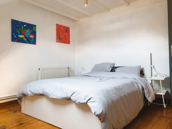 A bedroom with a bed, white walls, a radiator, and two paintings. - Family home in the heart of town (Calais)