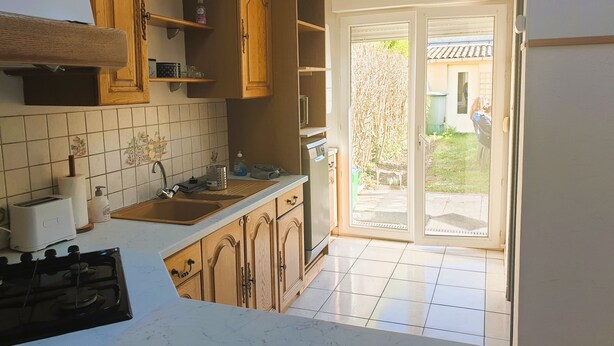 Une cuisine dotée de meubles en bois, d’une cuisinière à gaz, d’un évier et d’une porte-fenêtre coulissante donnant sur un patio.