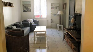 Un salon comprenant un canapé, une table basse, une lampe, un téléviseur et une bibliothèque.