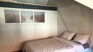 Une chambre à coucher comprenant un lit, une table de chevet et trois tableaux accrochés au mur, représentant une scène de plage.