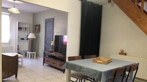 Un espace repas comprenant une table, des chaises, un téléviseur, une bibliothèque et une lampe.