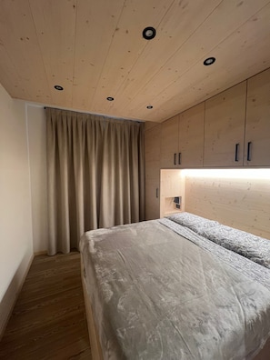 A bedroom with a bed, wooden ceiling, and a window with curtains. - Bormio Apartments al pradais giardino ovest (Bormio)