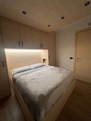 A bedroom with a bed, wooden headboard, and a door. - Bormio Apartments al pradais giardino ovest (Bormio)