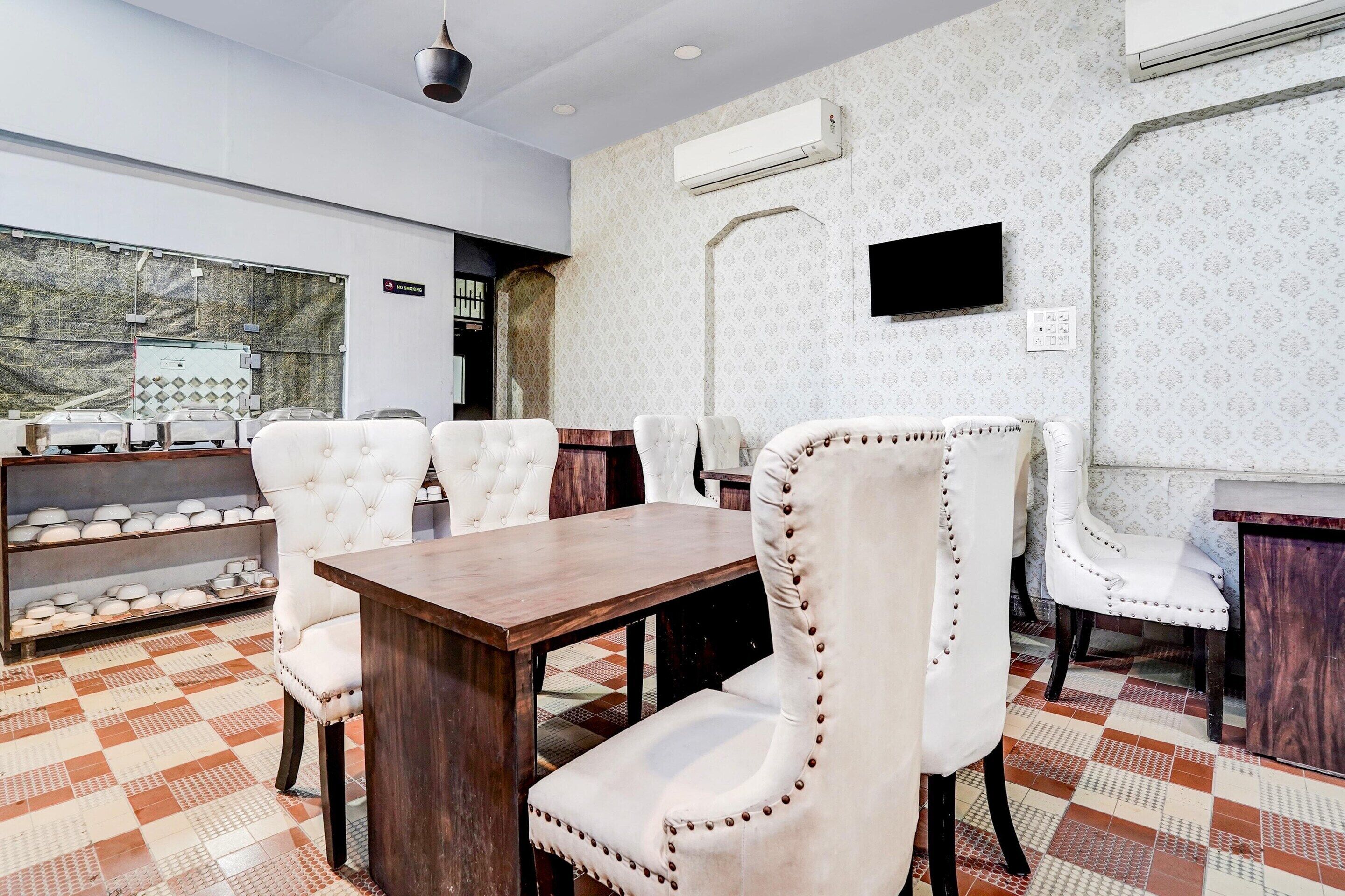 A dining area with a wooden table and white upholstered chairs, a patterned floor, and an air conditioning unit on the wall.