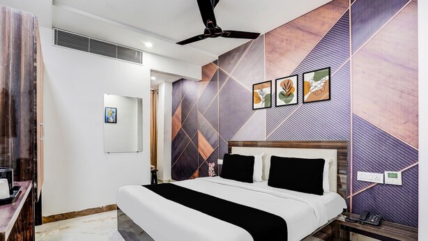 A hotel room with a bed, a ceiling fan, a nightstand, and a wall with geometric patterns. - Super Deluxe Room Golden Temple Amritsar A Star (Amritsar)