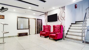 A hotel lobby with a tiled floor, a reception desk, a fire extinguisher, a staircase, and two red chairs. - Super Deluxe Room Golden Temple Amritsar A Star (Amritsar)