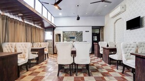 A hotel lobby with a checkered floor, white upholstered chairs, wooden tables, ceiling fans, and a TV mounted on the wall. - Super Deluxe Room Golden Temple Amritsar A Star (Amritsar)