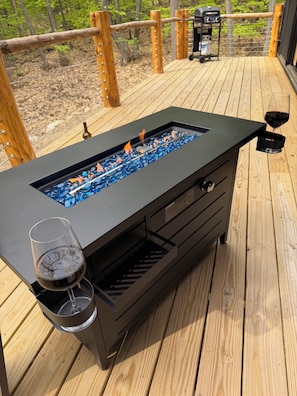 Un espace bar extĂ©rieur moderne, dotĂ© dâun barbecue intĂ©grĂ©, avec un verre de vin et une bouteille de vin posĂ©s sur une terrasse en bois.