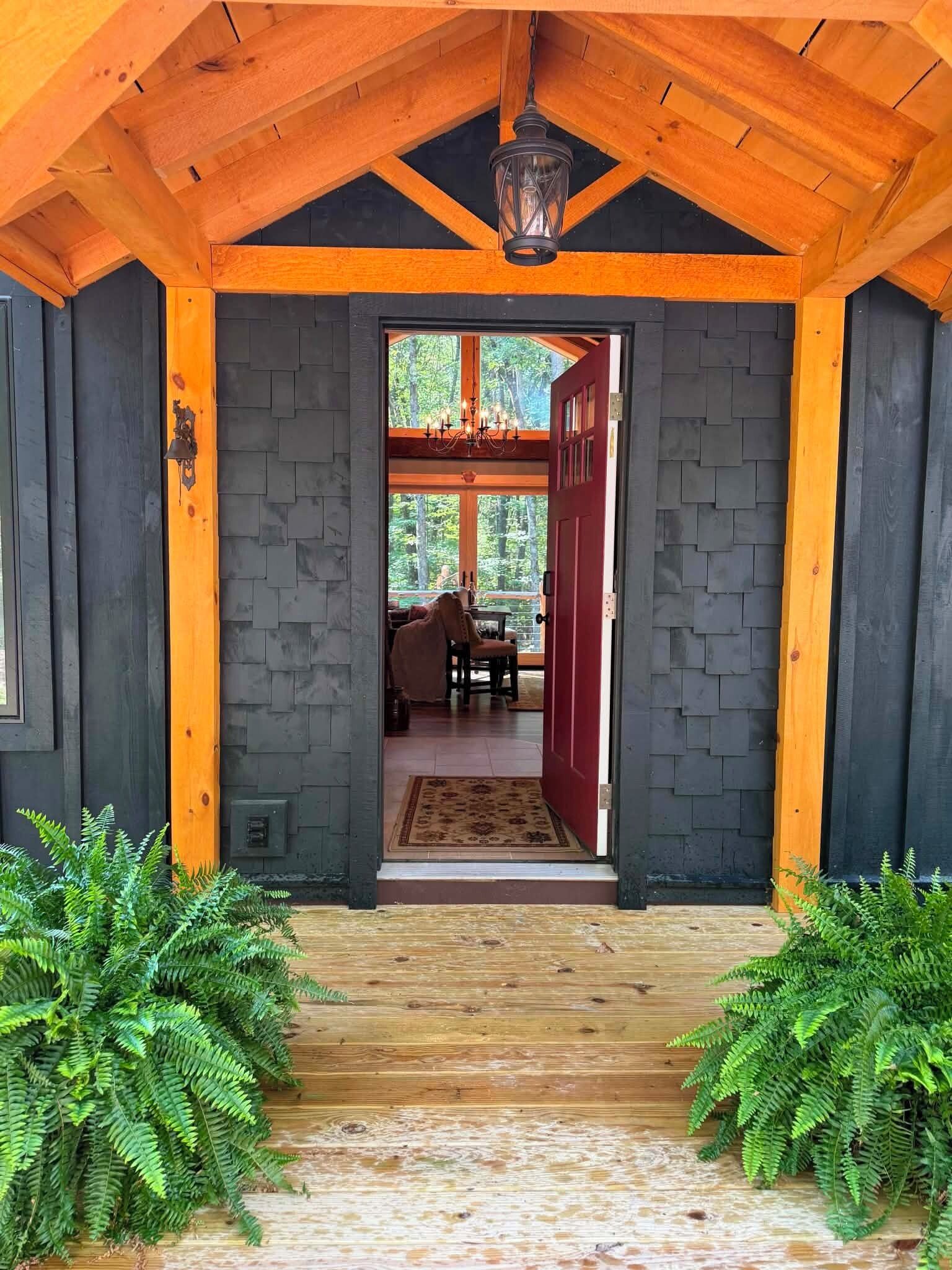 A wooden covered entrance with a red door, a chandelier, and a view into a room with a table and chairs.
