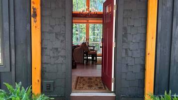 A wooden covered entrance with a red door, a chandelier, and a view into a room with a table and chairs.