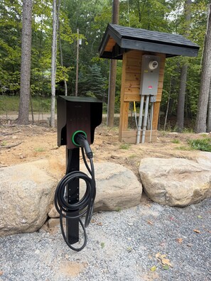 An outdoor electric vehicle charging station with a wooden structure in the background.