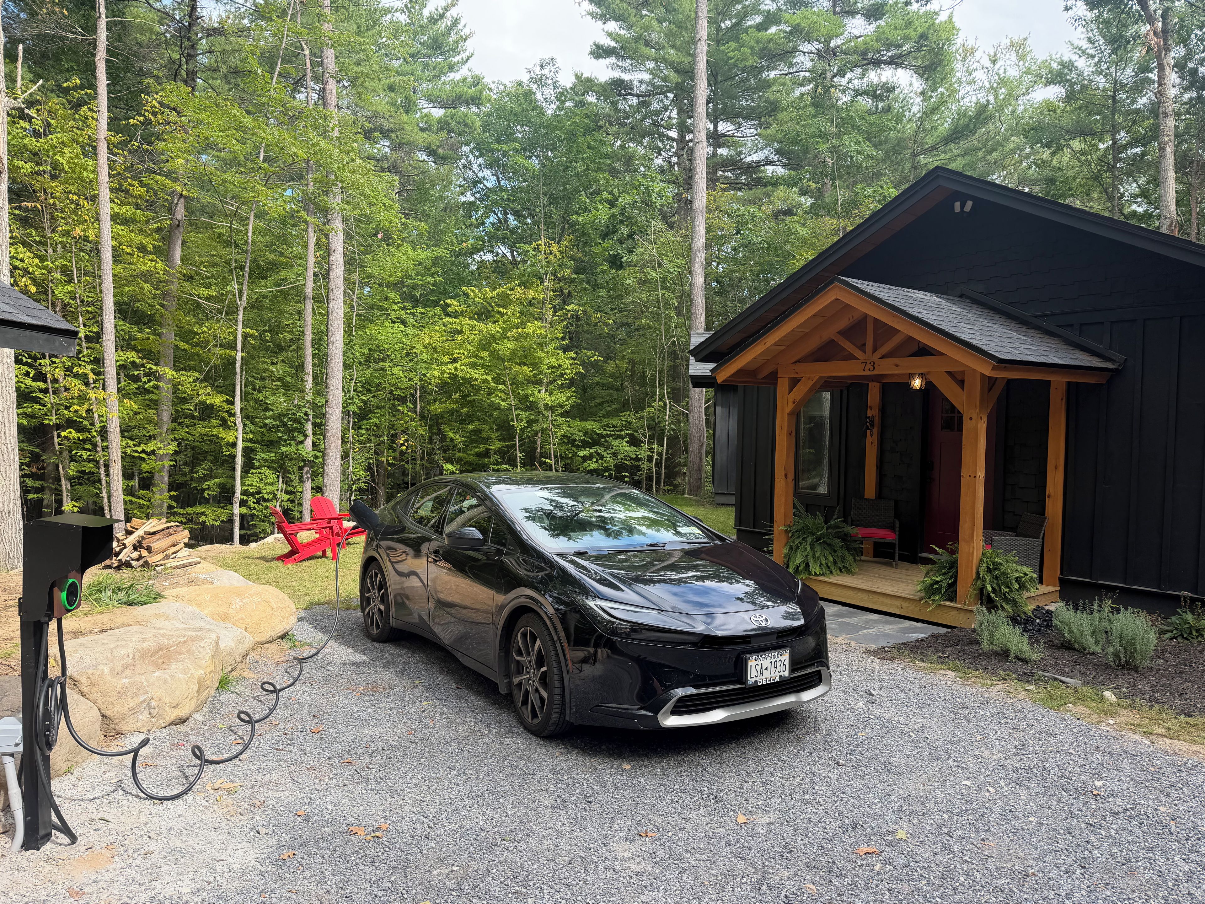A black car parked in front of a cabin with a porch, surrounded by a forest.