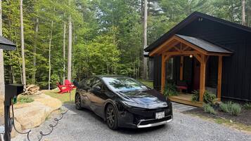 A black car parked in front of a cabin with a porch, surrounded by a forest.