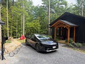 A black car parked in front of a cabin with a porch, surrounded by a forest.