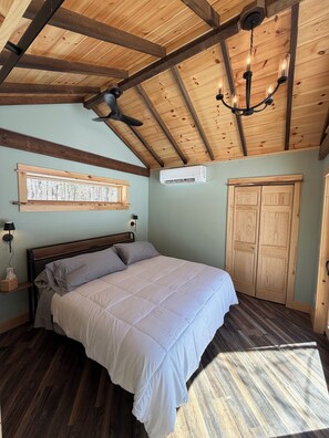 A bedroom with a bed, wooden ceiling beams, a ceiling fan, a window with a view, and a wardrobe. - Welcome to Onyx Chalet nestled in the heart of the Adirondacks (Jay)