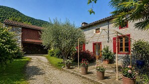 A stone house with a gravel path, potted plants, and a wooden pergola. - La Petite Maison - Spa - Games room - Air conditioning - Garden (Arguenos)