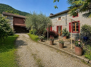 A stone house with a gravel path, potted plants, and a wooden pergola. - La Petite Maison - Spa - Games room - Air conditioning - Garden (Arguenos)