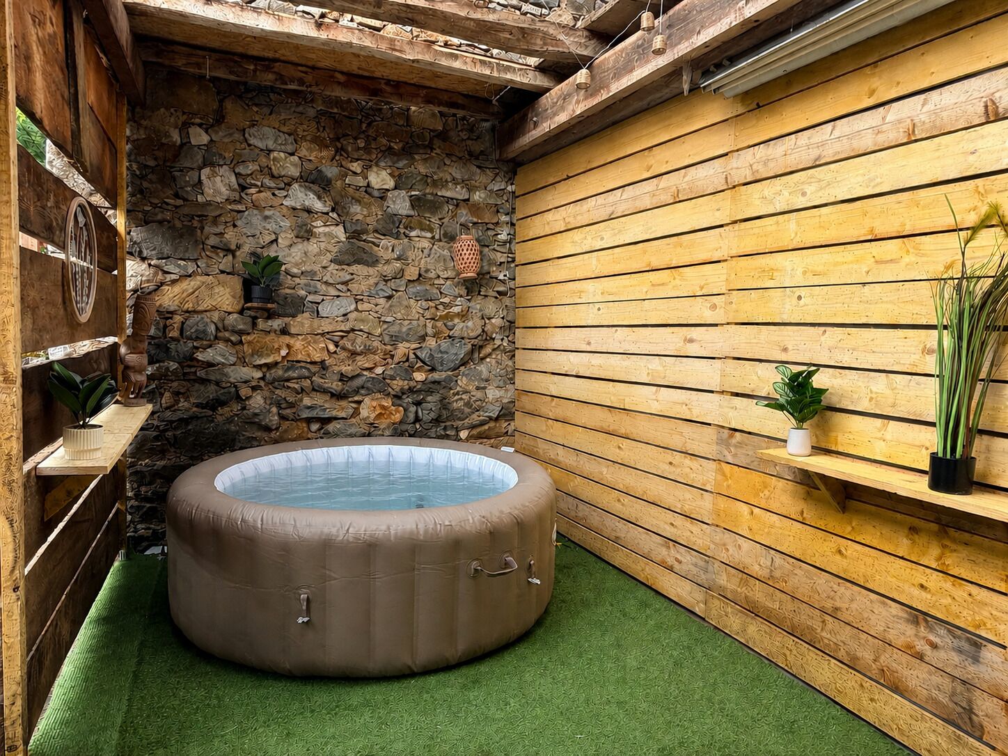 Ein Whirlpool in einem Raum mit Holzwänden, einer Steinwand und Kunstgrasanlage.