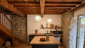 A rustic kitchen with wooden beams, a stone wall, and a wooden staircase. - La Petite Maison - Spa - Games room - Air conditioning - Garden (Arguenos)