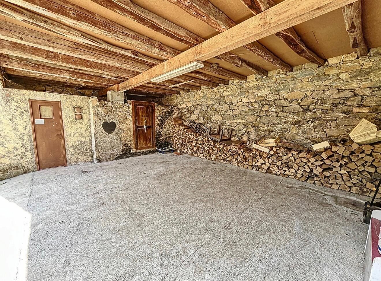 Une pièce aux murs de pierre, avec un plafond en bois, une porte et une pile de bois de chauffage.