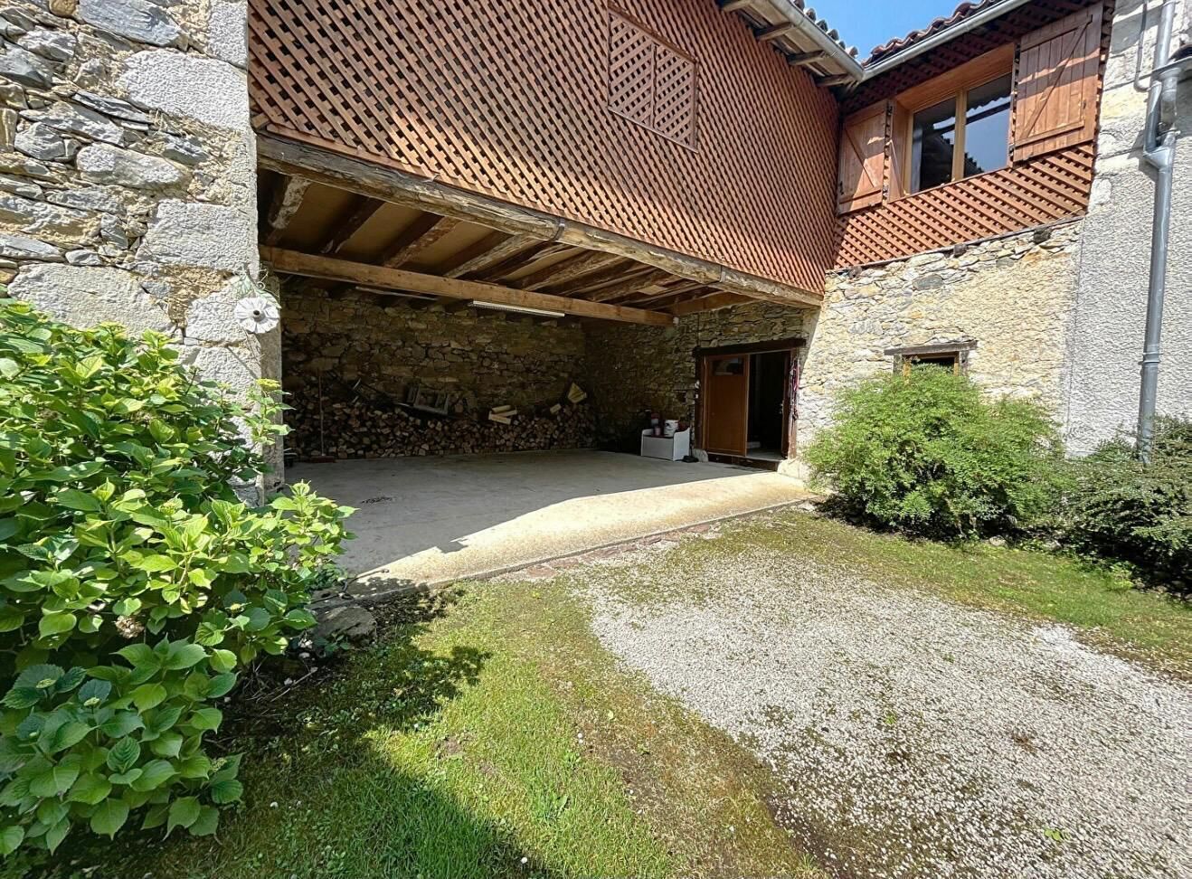 Un bâtiment en pierre agrémenté d’une pergola en bois, d’un chemin de gravier et d’arbustes verts.