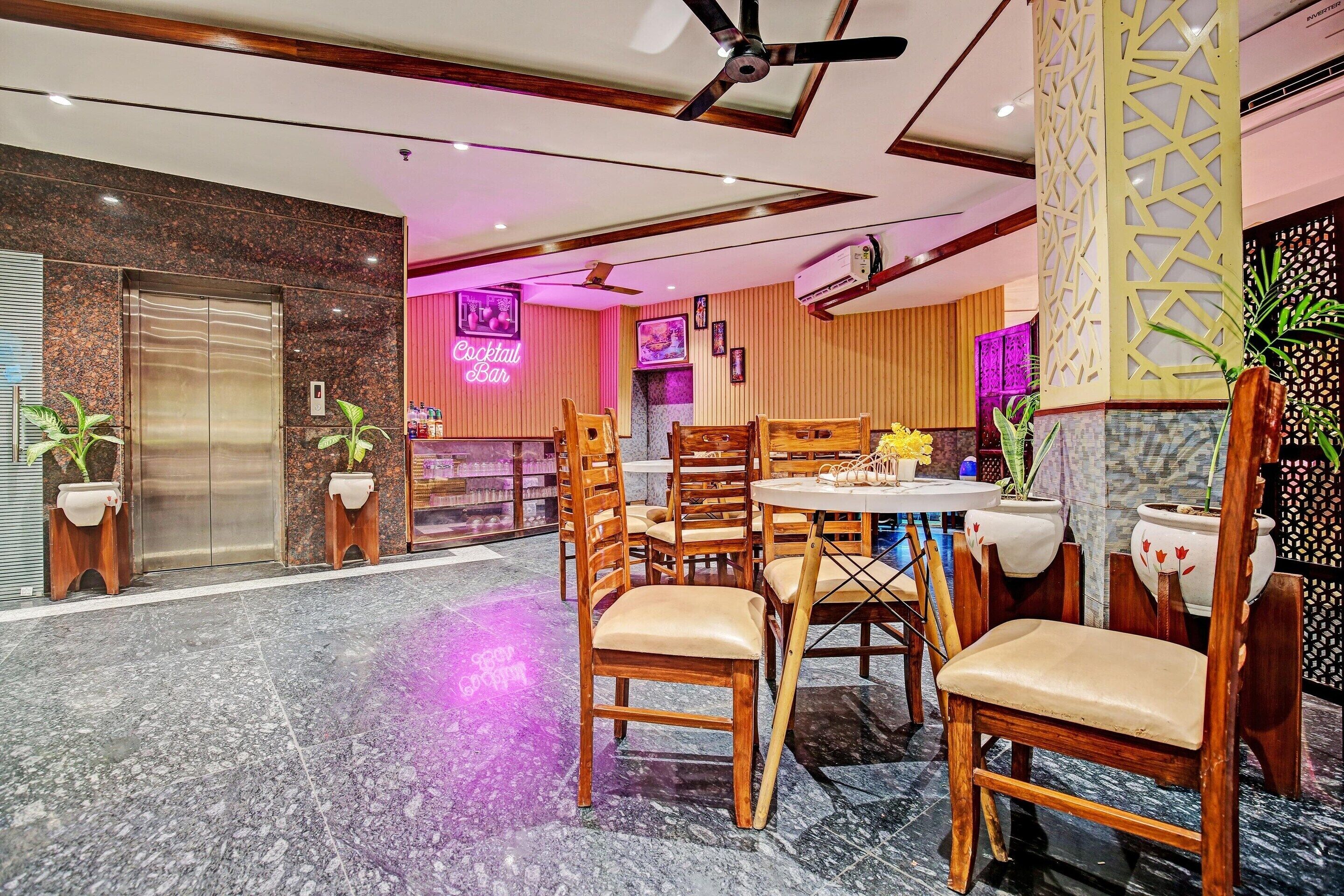 A hotel lobby with a marble floor, wooden chairs, a ceiling fan, and a neon sign for a cocktail bar.