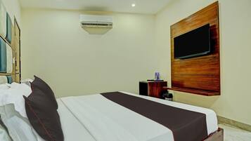 Hotelkamer met een bed, een wandtelevisie, een airconditioning en een klein tafeltje met een fles water.