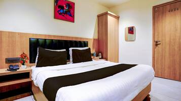 A hotel room with a large bed, a wooden headboard, a nightstand with a phone and a vase of flowers, and a painting on the wall.
