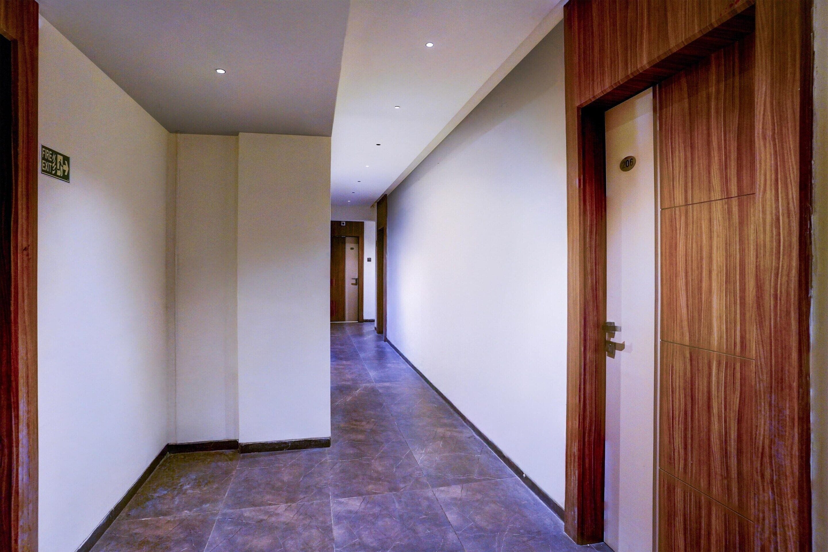A corridor with a wooden door on the right, a sign indicating an exit on the left, and a tiled floor.