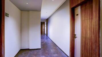 A corridor with a wooden door on the right, a sign indicating an exit on the left, and a tiled floor.
