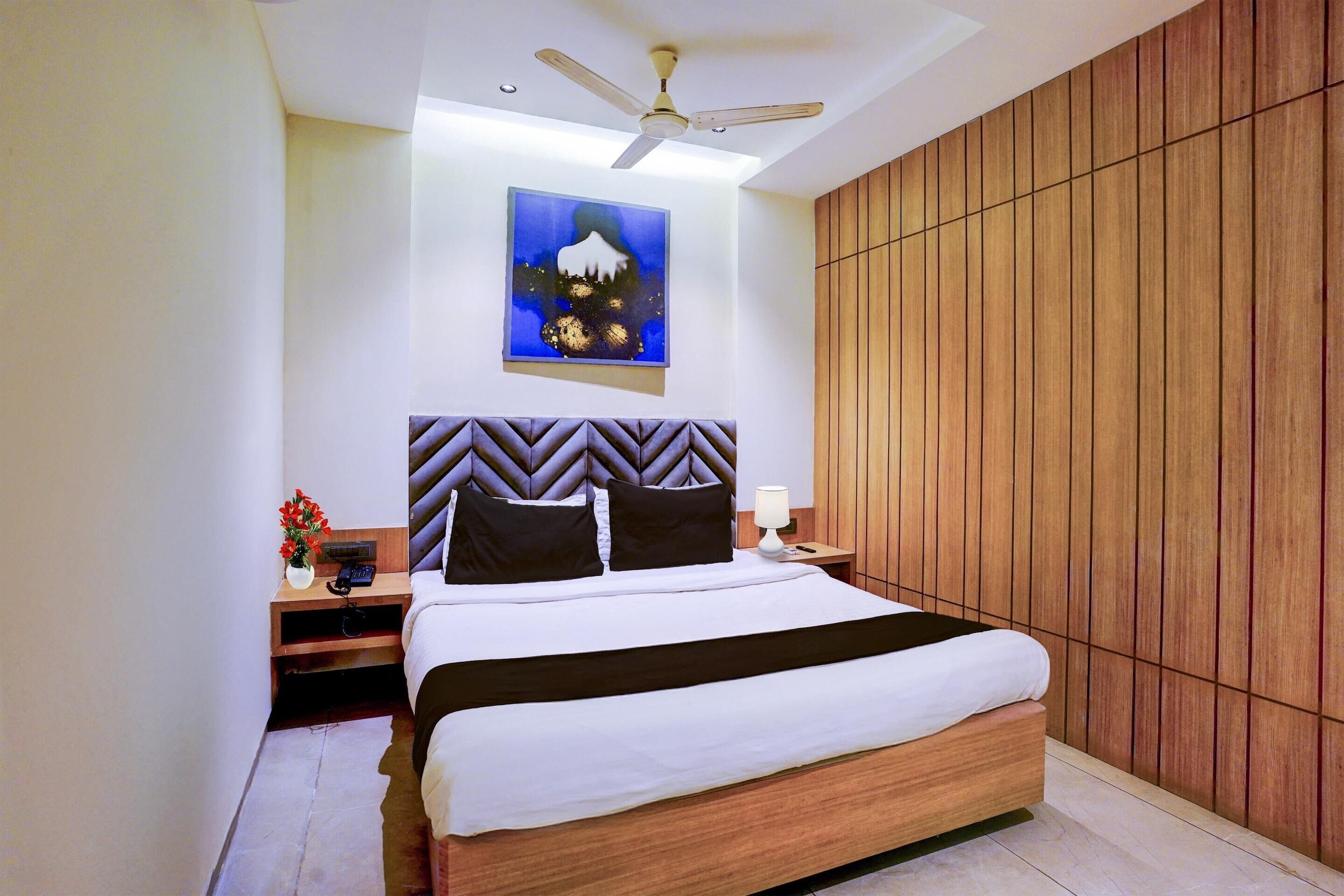 A bedroom with a bed, a nightstand, a lamp, a ceiling fan, and a wooden panel wall.