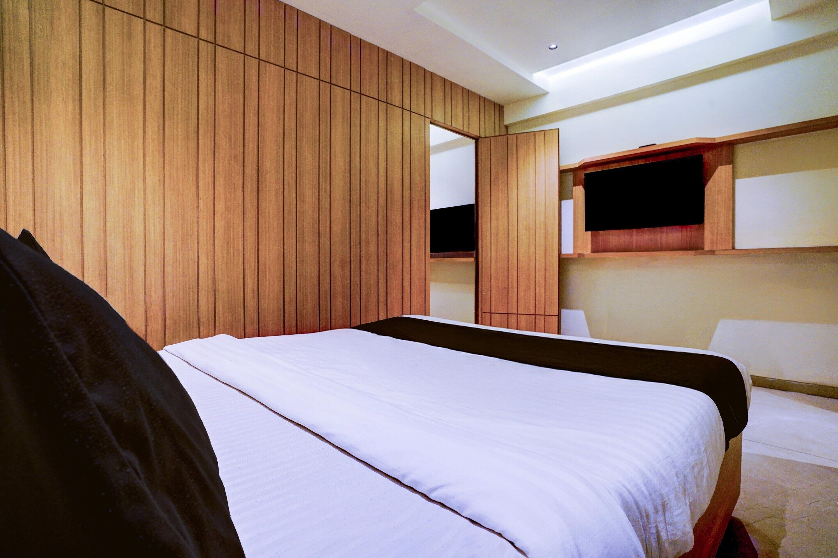 A modern hotel room with a large bed, wooden panel walls, a built-in TV, and a small seating area.