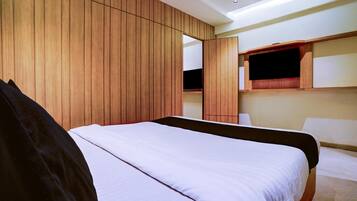 A modern hotel room with a large bed, wooden panel walls, a built-in TV, and a small seating area.