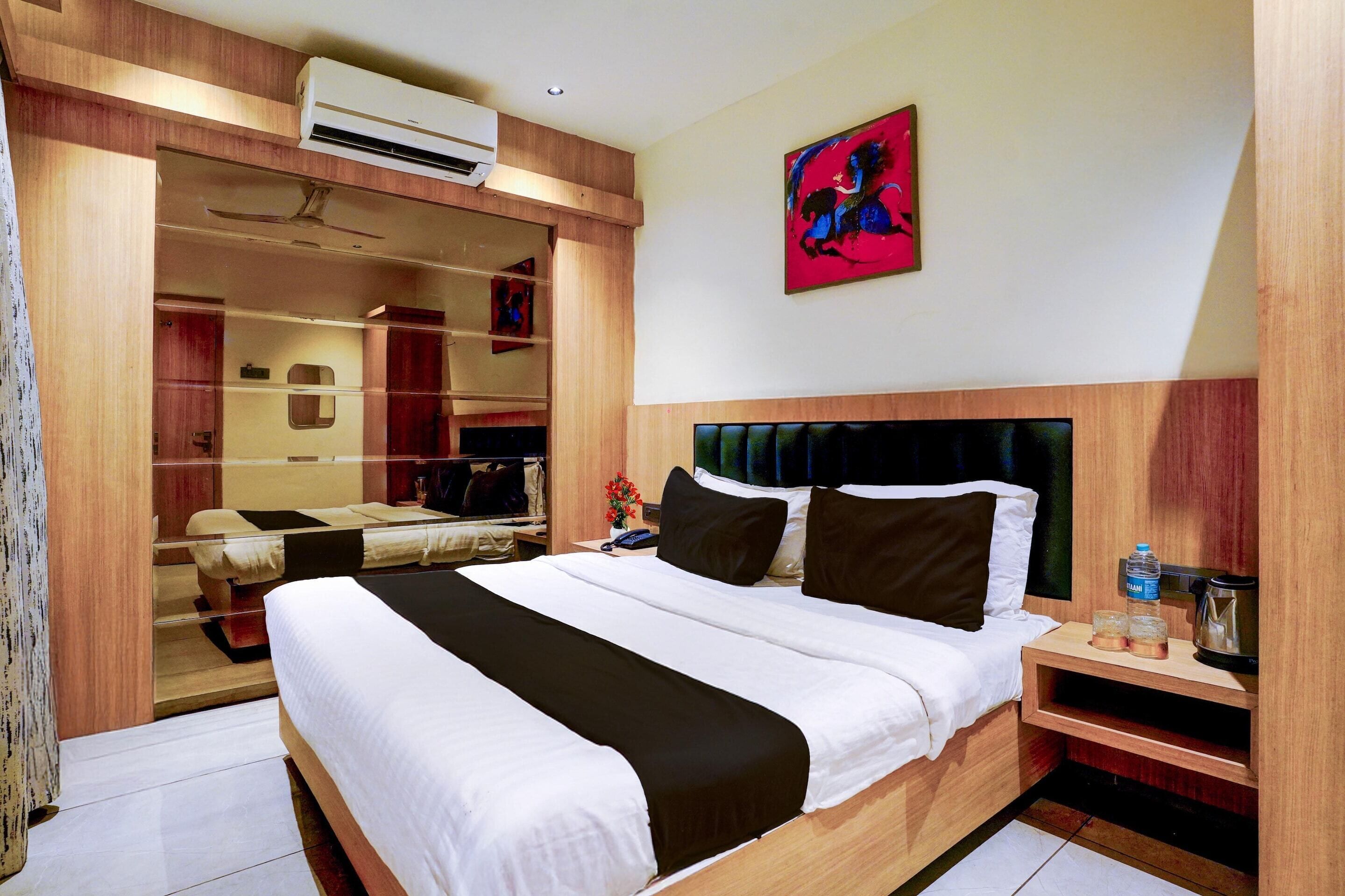 Ein Hotelzimmer mit einem großen Bett, einem Kleiderschrank, einem Spiegel, einem Bild an der Wand und einer Klimaanlage.