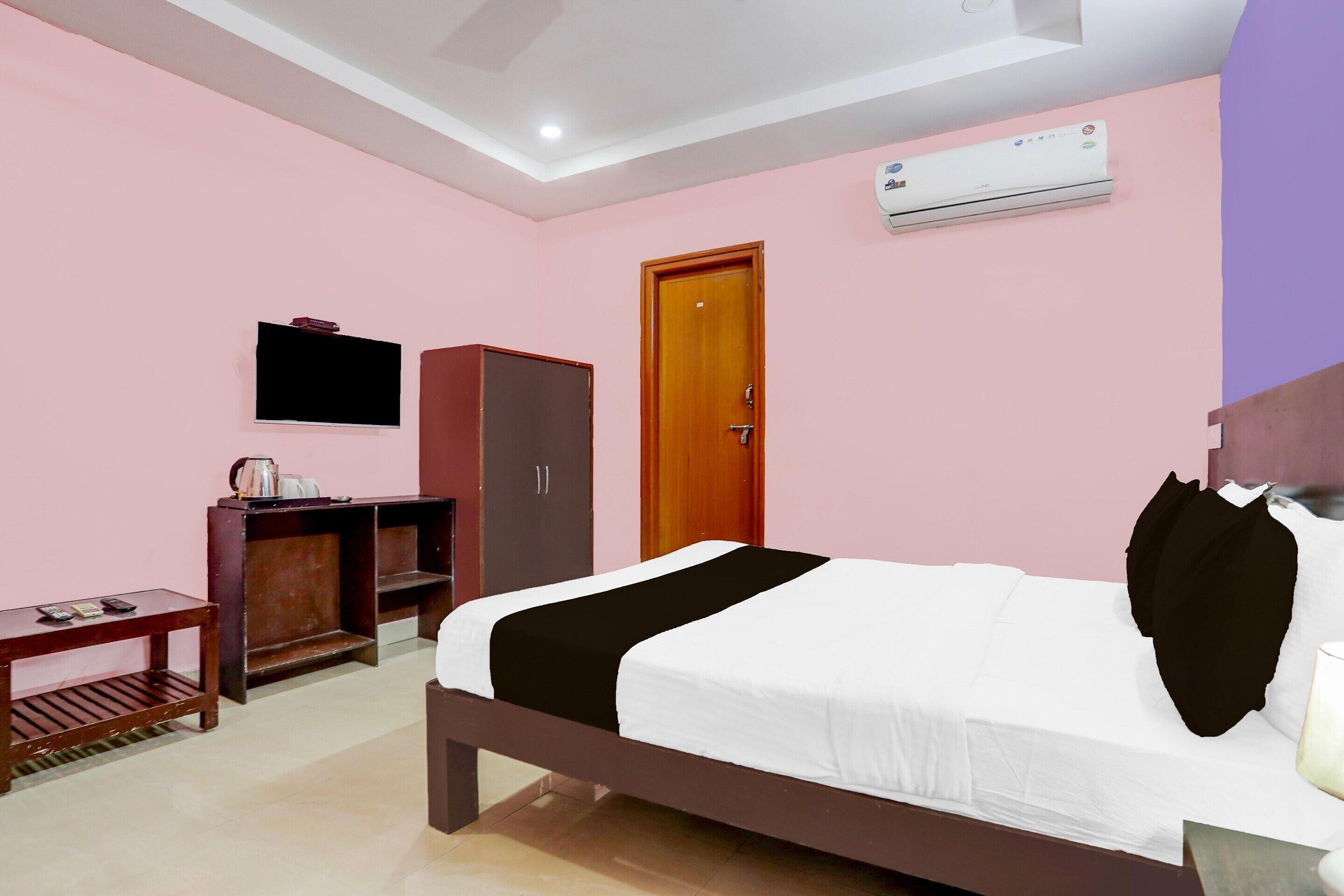 A bedroom with a bed, a wardrobe, a television, and an air conditioning unit.