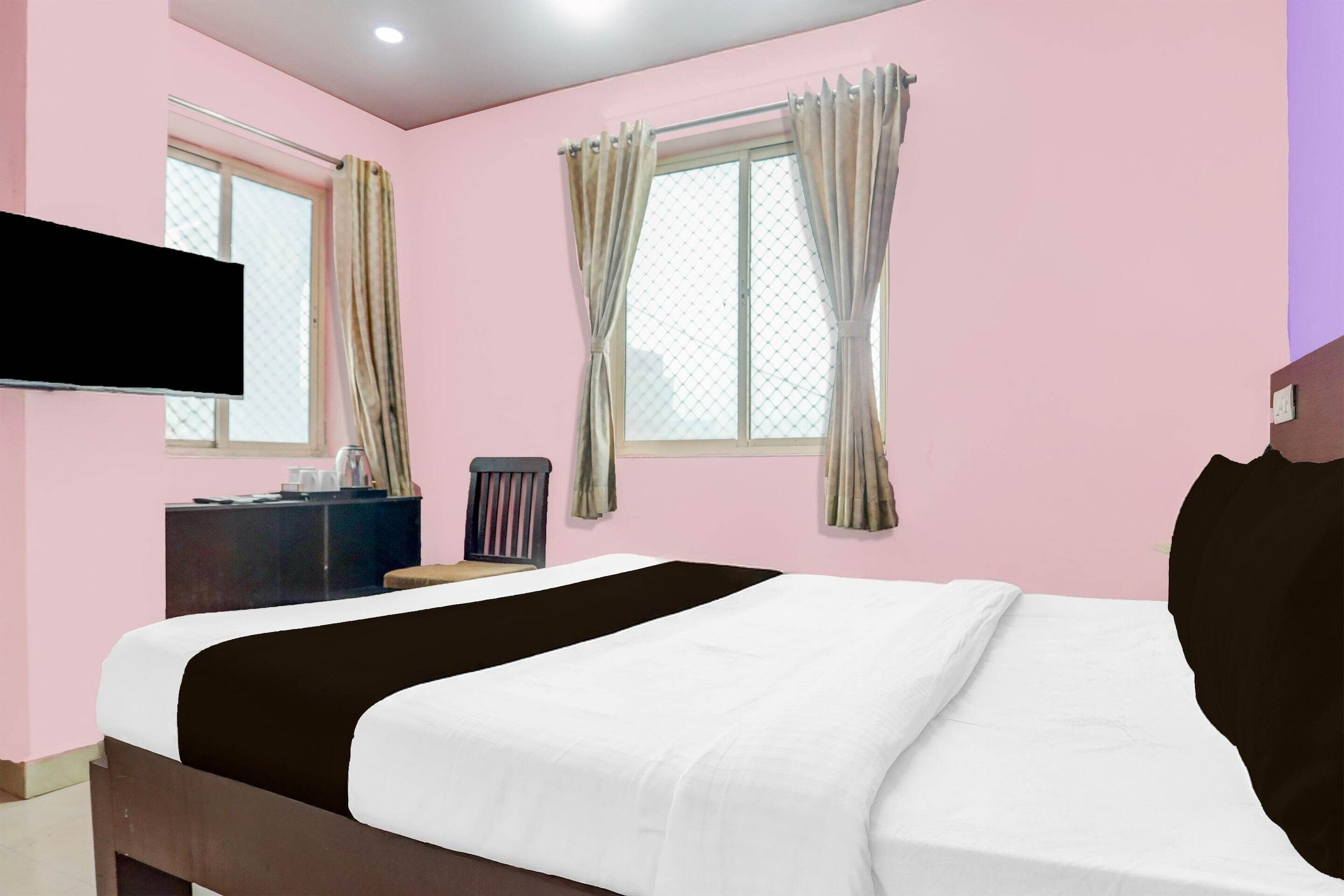 A hotel room with a bed, a TV mounted on the wall, a window with curtains, and a dresser.