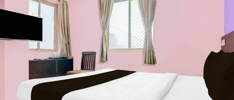 A hotel room with a bed, a TV mounted on the wall, a window with curtains, and a dresser.