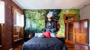 A bedroom with a brick wall, a large bed with a red rug, and a mural of a train on the wall. - New! The Old Timer - 5BR/4.5BA - Hot Tub! Historic! (Louisville)