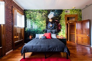 Ein Schlafzimmer mit Backsteinwand, einem großen Bett und einem roten Teppich, sowie einem Wandgemälde eines Zuges.