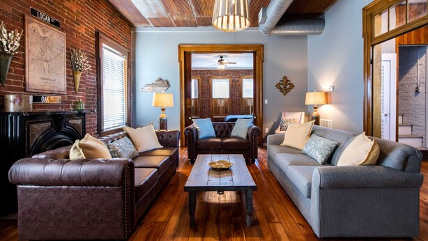 A cozy living room with leather sofas, a wooden coffee table, and a brick wall. - New! The Old Timer - 5BR/4.5BA - Hot Tub! Historic! (Louisville)
