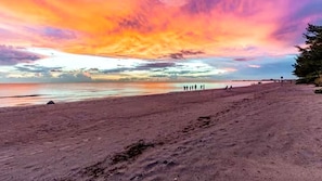 Ein Strand bei Sonnenuntergang, Menschen schlendern herum, und der Himmel ist klar.
